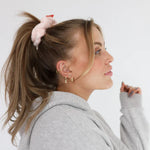 Woman in a gray hoodie wearing the Kaxi Midi Towel Scrunchie in blush pink in a high ponytail