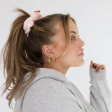 Woman in a gray hoodie wearing the Kaxi Midi Towel Scrunchie in blush pink in a high ponytail