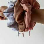 Hand holding a bundle of Kaxi Oversized Workout Scrunchies in brown, blue and blush