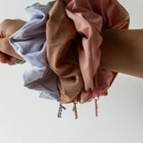 Hand holding a bundle of Kaxi Oversized Workout Scrunchies in brown, blue and blush