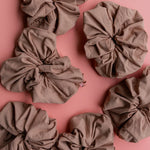 Kaxi Oversized Workout Scrunchies in Nude brown scattered on a pink background