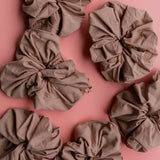 Kaxi Oversized Workout Scrunchies in Nude brown scattered on a pink background