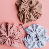 Kaxi Oversized Workout Scrunchies in blush, brown and soft blue scattered on a pink background