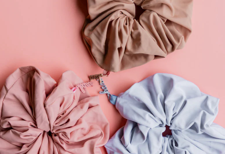 Kaxi Oversized Workout Scrunchies in blush, brown and soft blue scattered on a pink background
