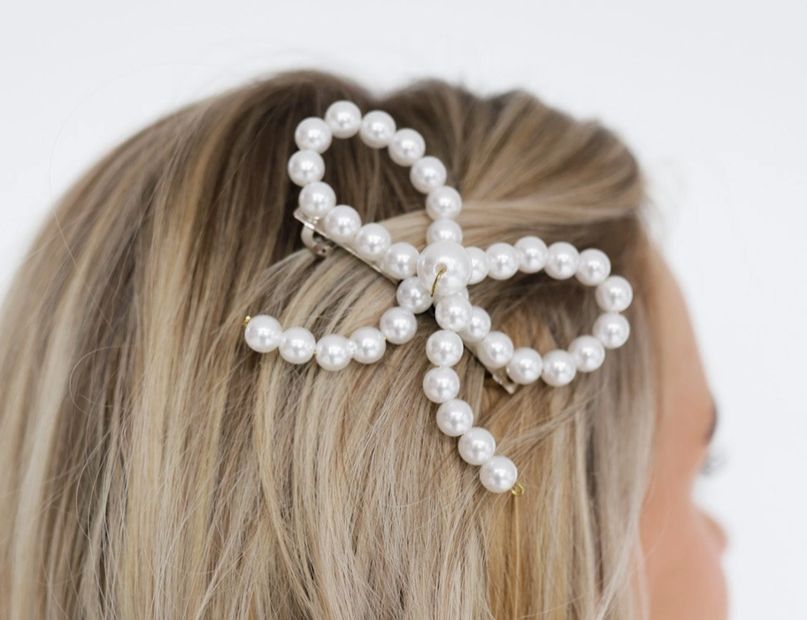 Kaxi Pearl Barrette, a pearl bow-shaped hair clip worn in blonde hair