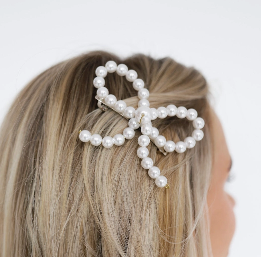 Kaxi Pearl Barrette, a pearl bow-shaped hair clip worn in blonde hair