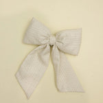 Kaxi Puffy Bow in Blossom, a cream textured fabric bow with long tails, laid flat