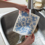 Hands rinsing a blue-printed Kei & Molly Sponge Cloth under a kitchen faucet