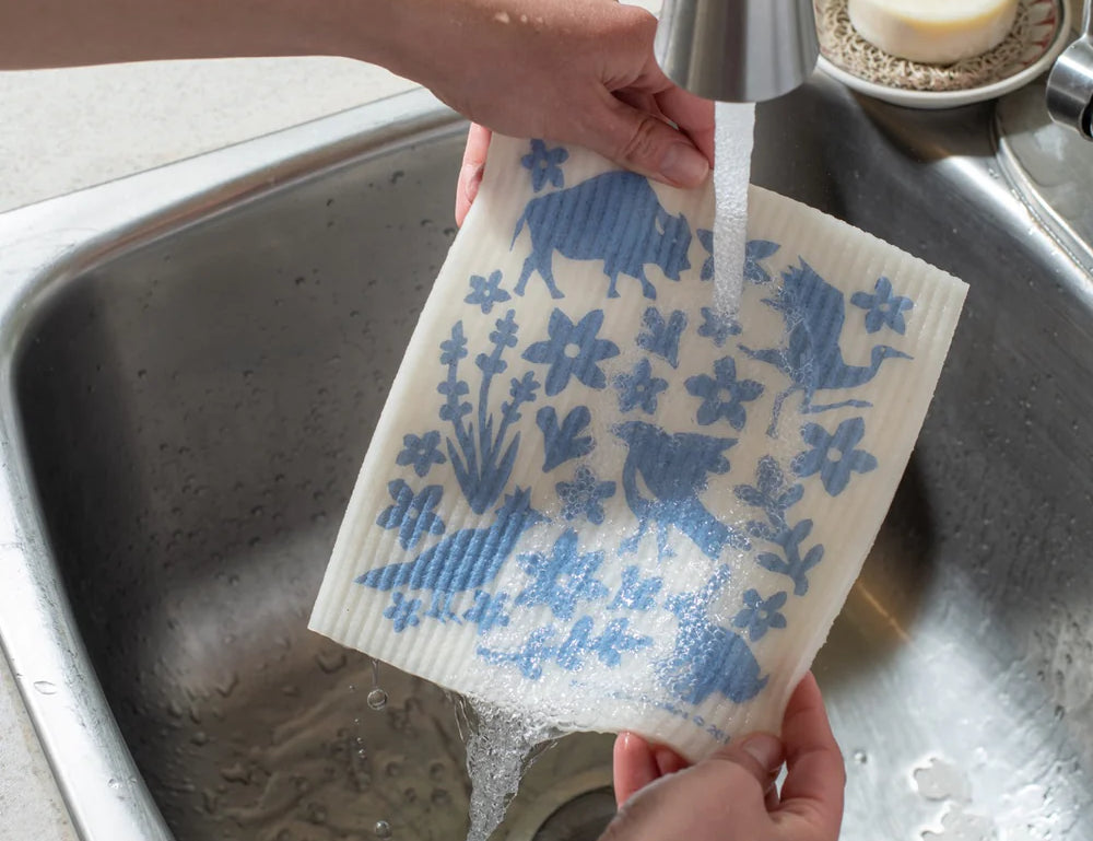 Hands rinsing a blue-printed Kei & Molly Sponge Cloth under a kitchen faucet