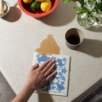 Hand wiping a counter with a blue-printed Kei & Molly Sponge Cloth