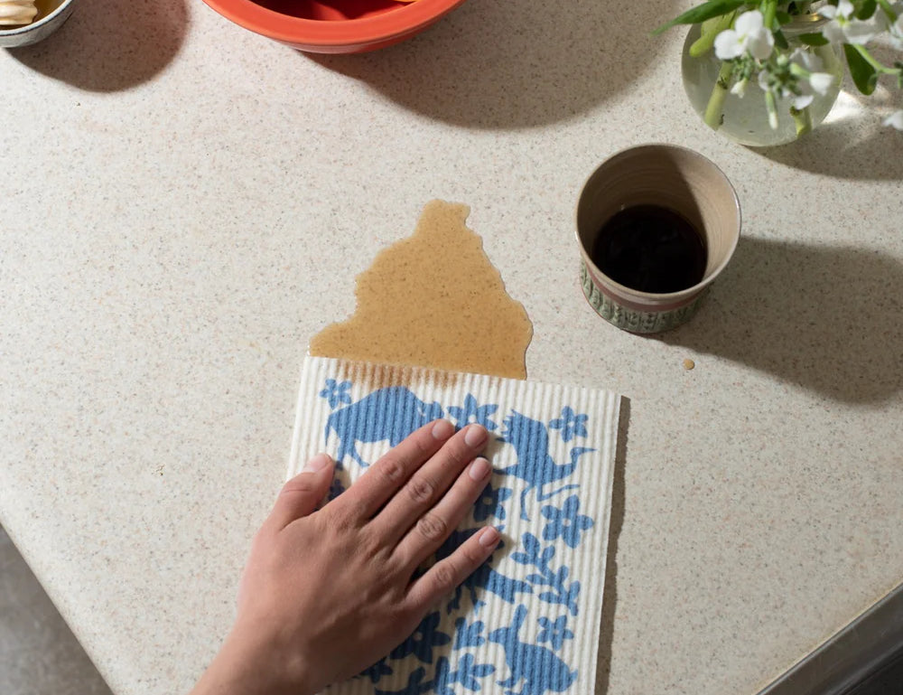 Hand wiping a counter with a blue-printed Kei & Molly Sponge Cloth