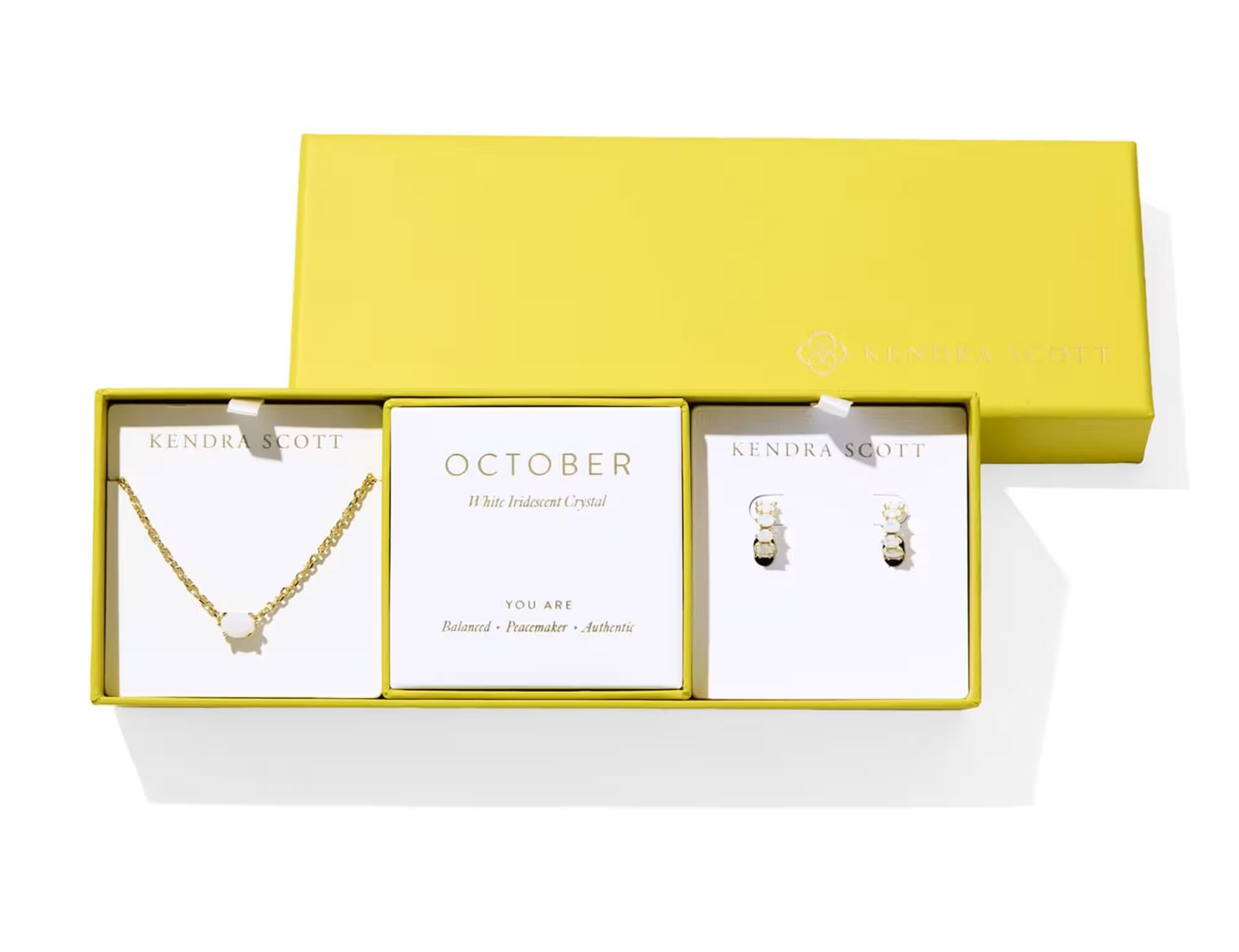 Kendra Scott Cailin Birthstone Gift Set for October in gold with White Iridescent Crystal, a pendant necklace and huggie earrings in a yellow gift box