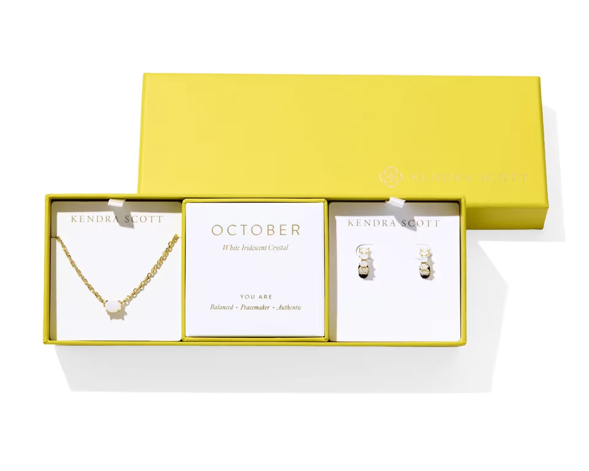 Kendra Scott Cailin Birthstone Gift Set for October in gold with White Iridescent Crystal, a pendant necklace and huggie earrings in a yellow gift box