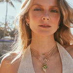 Woman in a cream halter top layering the Kendra Scott Cailin Gold Birthday Pendant Necklace with gold charms