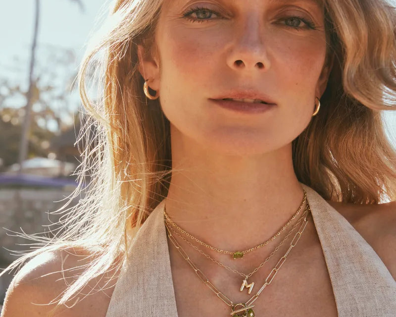 Woman in a cream halter top layering the Kendra Scott Cailin Gold Birthday Pendant Necklace with gold charms