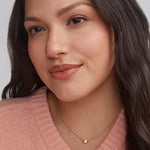 Woman in a pink sweater wearing the Kendra Scott Cailin Gold Birthday Pendant Necklace