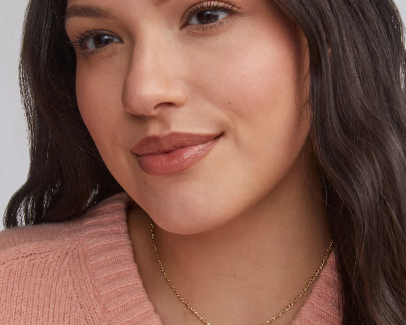 Woman in a pink sweater wearing the Kendra Scott Cailin Gold Birthday Pendant Necklace