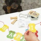 Hands assembling the Kikkerland Dog Birthday Kit banner with a small black dog watching