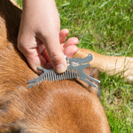 Hand using the Kikkerland Tick Tool comb on a dog's fur outdoors