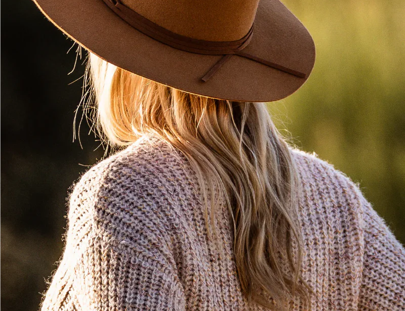 Woman in a knit sweater at golden hour wearing the Kooringal Alice Wide Brim Fedora in Tan, back view