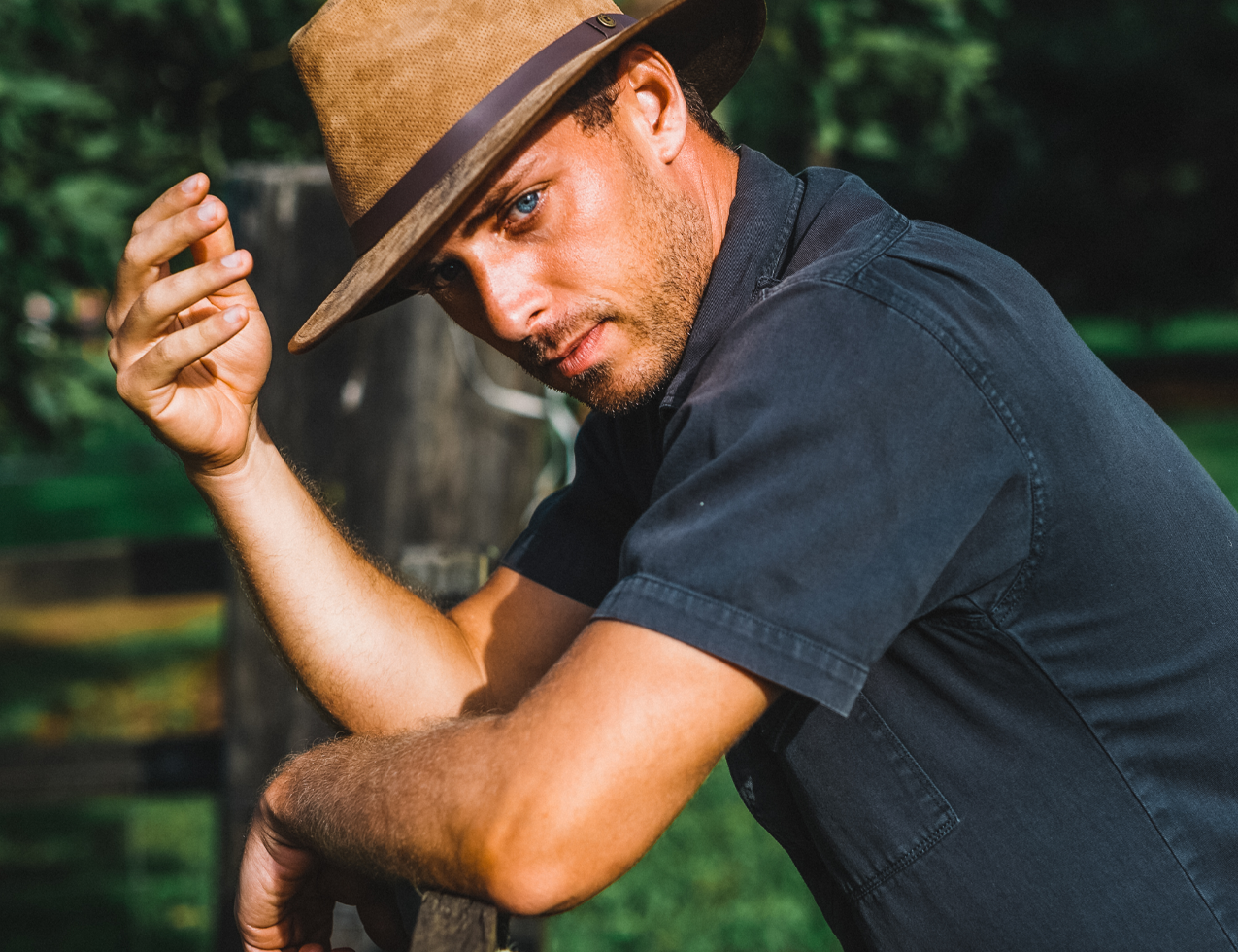 Man leaning on a fence wearing the Kooringal Canungra Drover hat in Tan