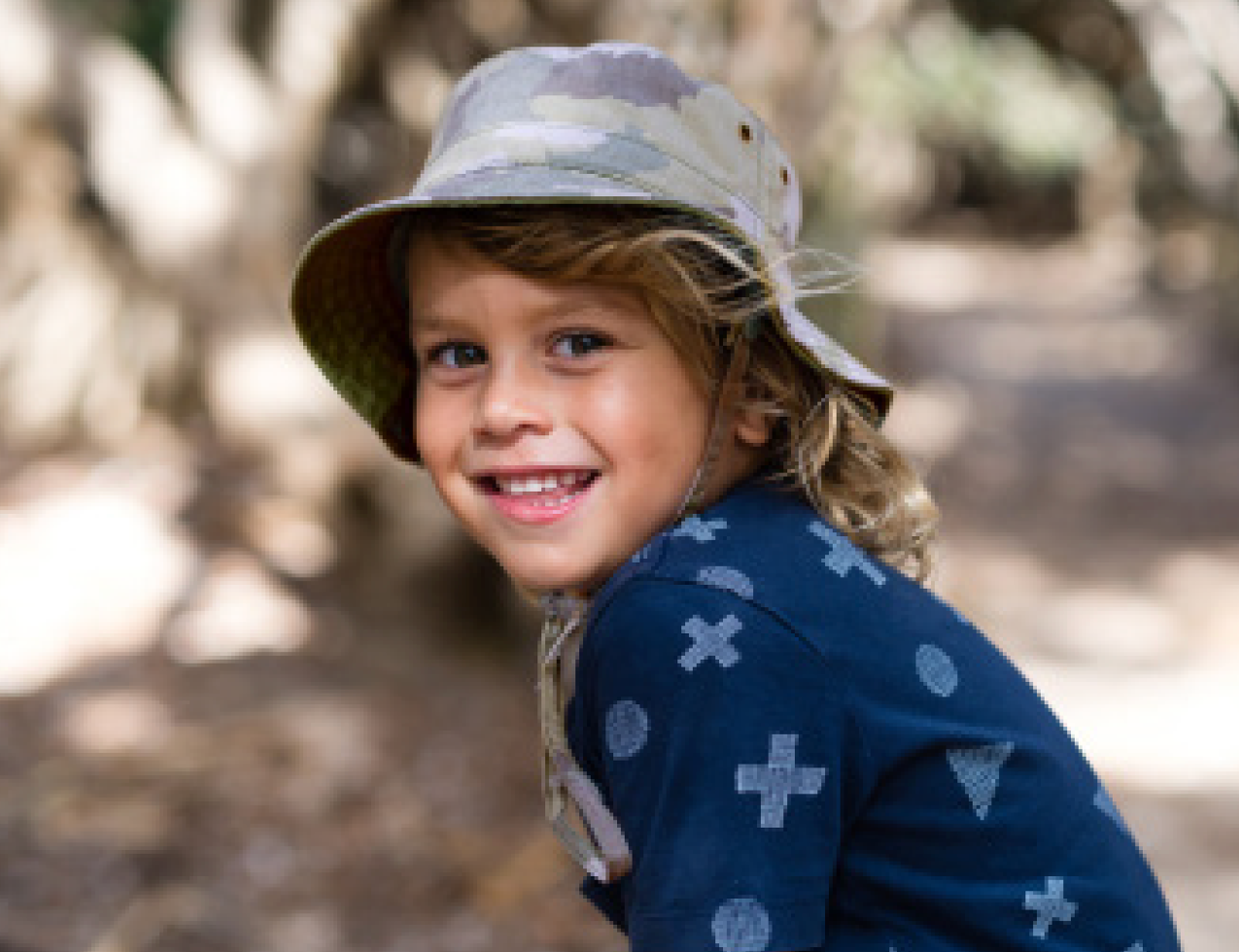 Boy wearing the Kooringal Dozer Boys Bucket Hat in Camo outdoors under trees