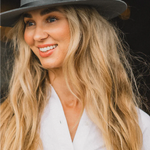 Smiling woman with long blonde hair wearing the Kooringal Goodwin Wide Brim Fedora in Driftwood