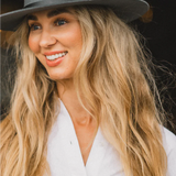 Smiling woman with long blonde hair wearing the Kooringal Goodwin Wide Brim Fedora in Driftwood