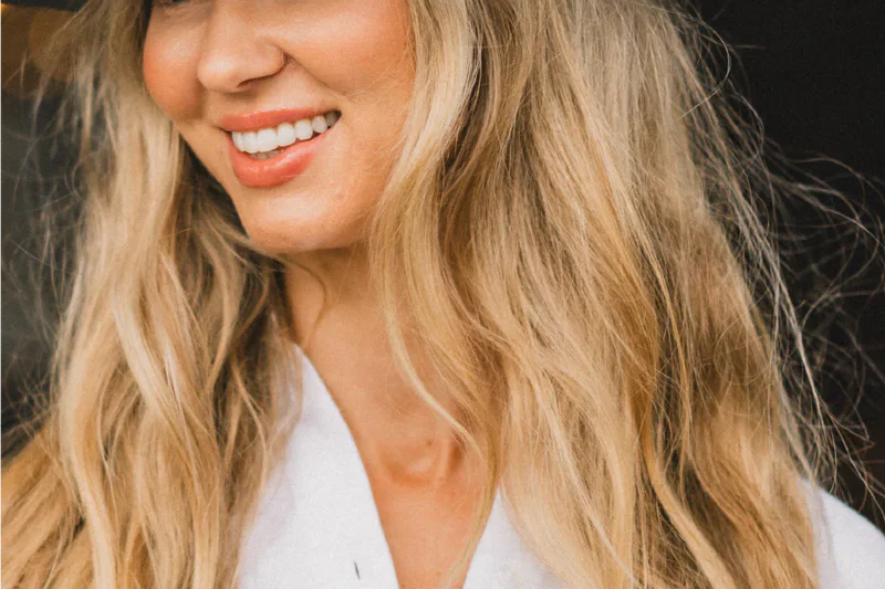Smiling woman with long blonde hair wearing the Kooringal Goodwin Wide Brim Fedora in Driftwood