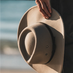 Hand holding the Kooringal Nomad Cowboy Hat in Sand with the brim in soft light