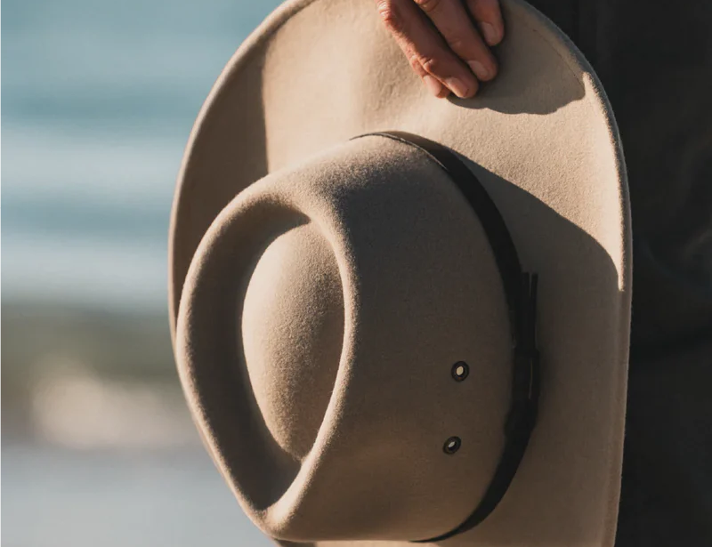 Hand holding the Kooringal Nomad Cowboy Hat in Sand with the brim in soft light
