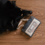Black dog sniffing the Lambwolf Collective Cassette Dog Toy on a wood floor