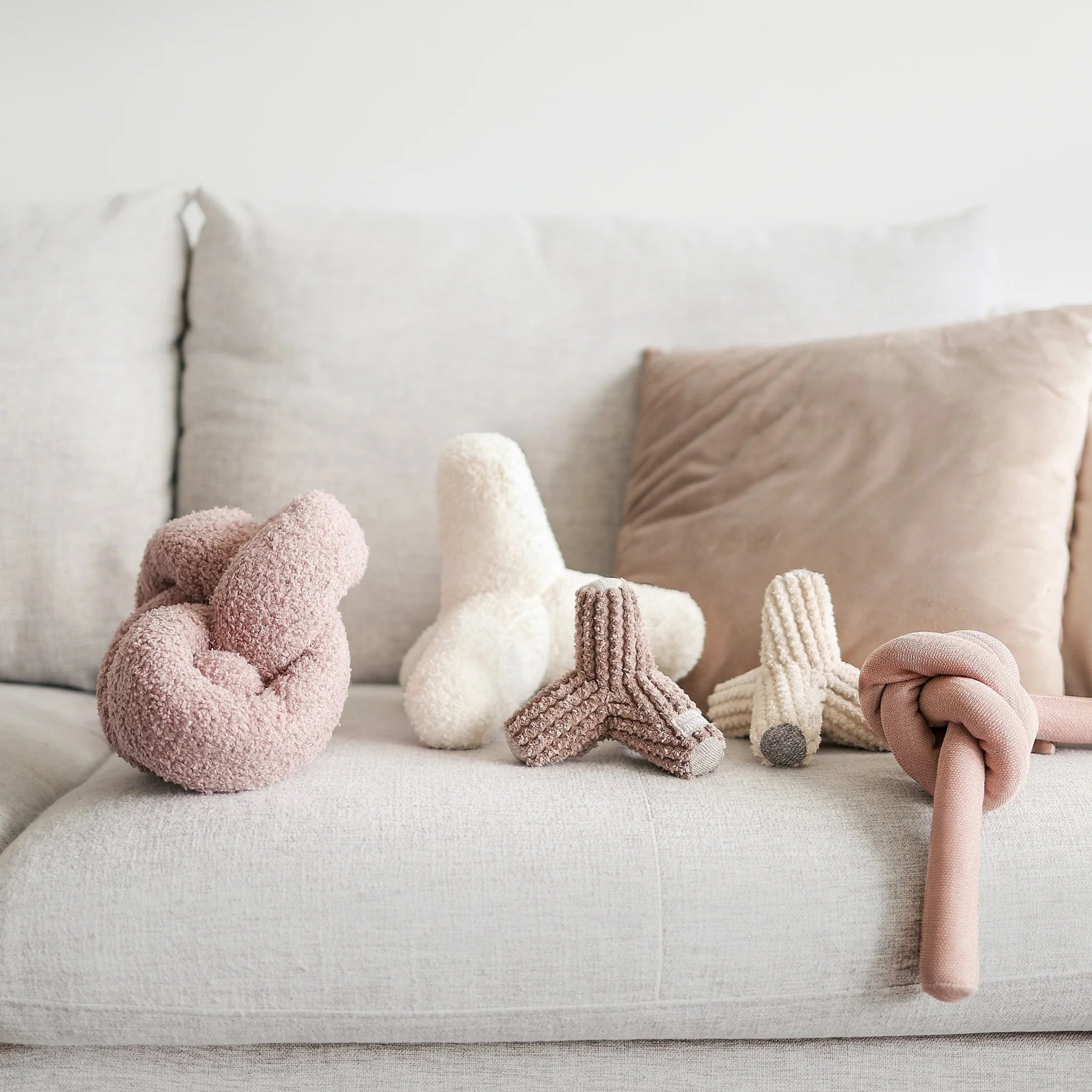 Lambwolf Collective Nounou Dogwood Squeakers Dog Toys in blush and cream on a gray couch