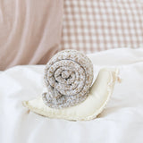 Lambwolf Collective Snail Snuffle Dog Toy on a white pillow with gingham bedding