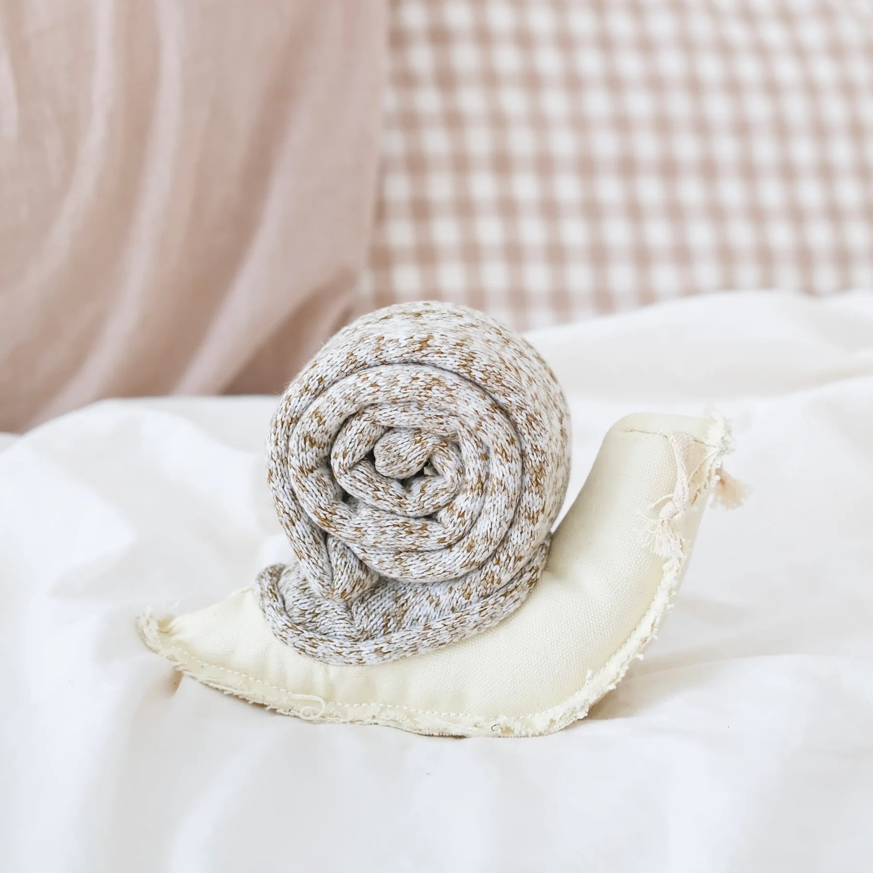 Lambwolf Collective Snail Snuffle Dog Toy on a white pillow with gingham bedding