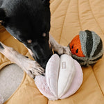 Black dog pawing at the Lambwolf Collective Toto Enrichment Dog Toy in Pink on a mustard blanket