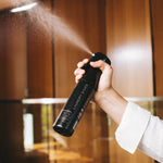 Hand spraying the Laundry Sauce Fabric Refresher Spray in a wood-paneled closet