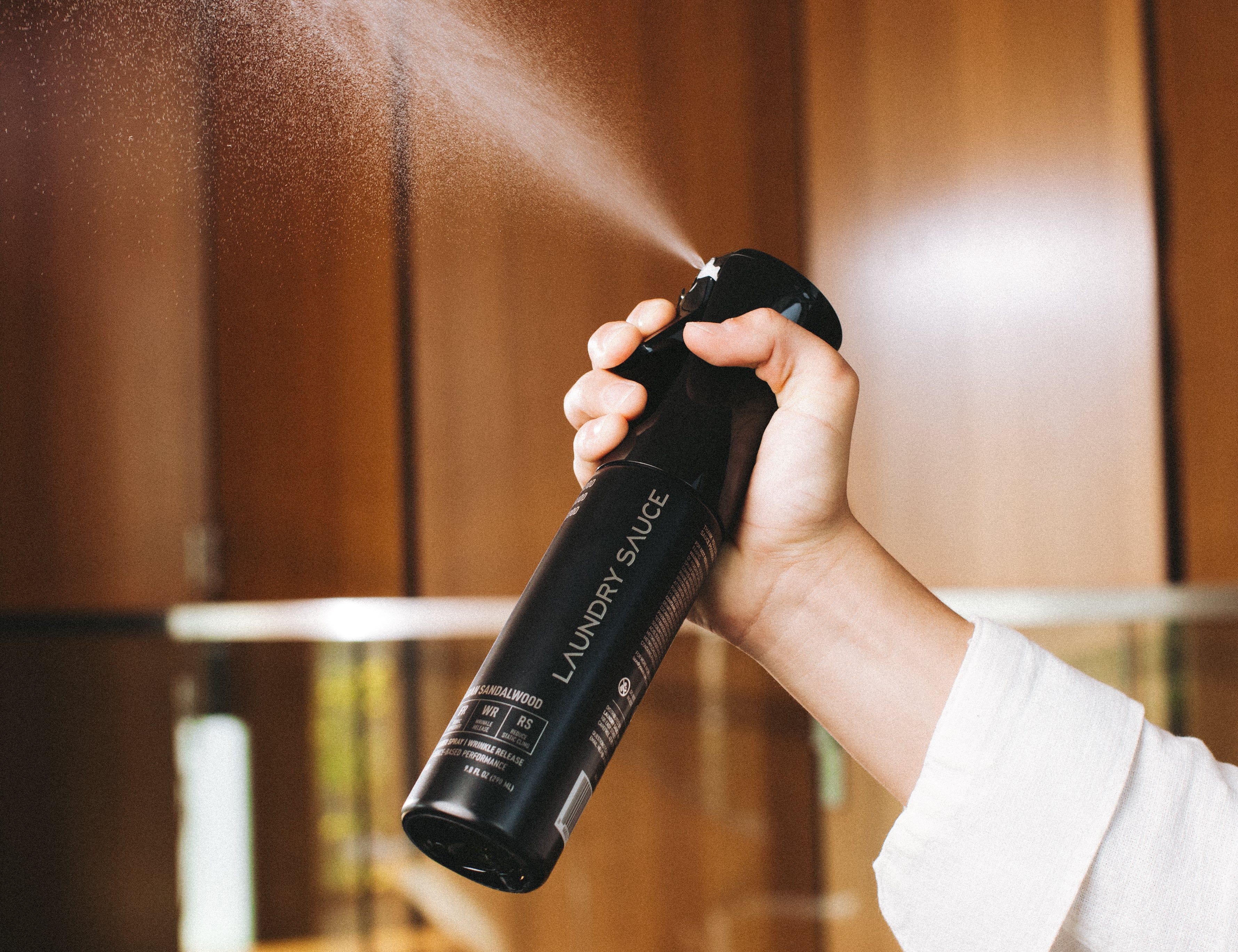 Hand spraying the Laundry Sauce Fabric Refresher Spray in a wood-paneled closet