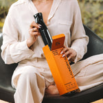 Woman in a cream outfit holding the Laundry Sauce Fabric Refresher Spray and its orange box