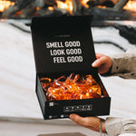 Hands holding an open black box of Laundry Sauce Laundry Detergent Pods by a fireplace