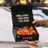 Hands holding an open black box of Laundry Sauce Laundry Detergent Pods by a fireplace