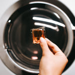 Hand dropping a Laundry Sauce Laundry Detergent Pod into a washing machine drum