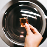 Hand dropping a Laundry Sauce Laundry Detergent Pod into a washing machine drum