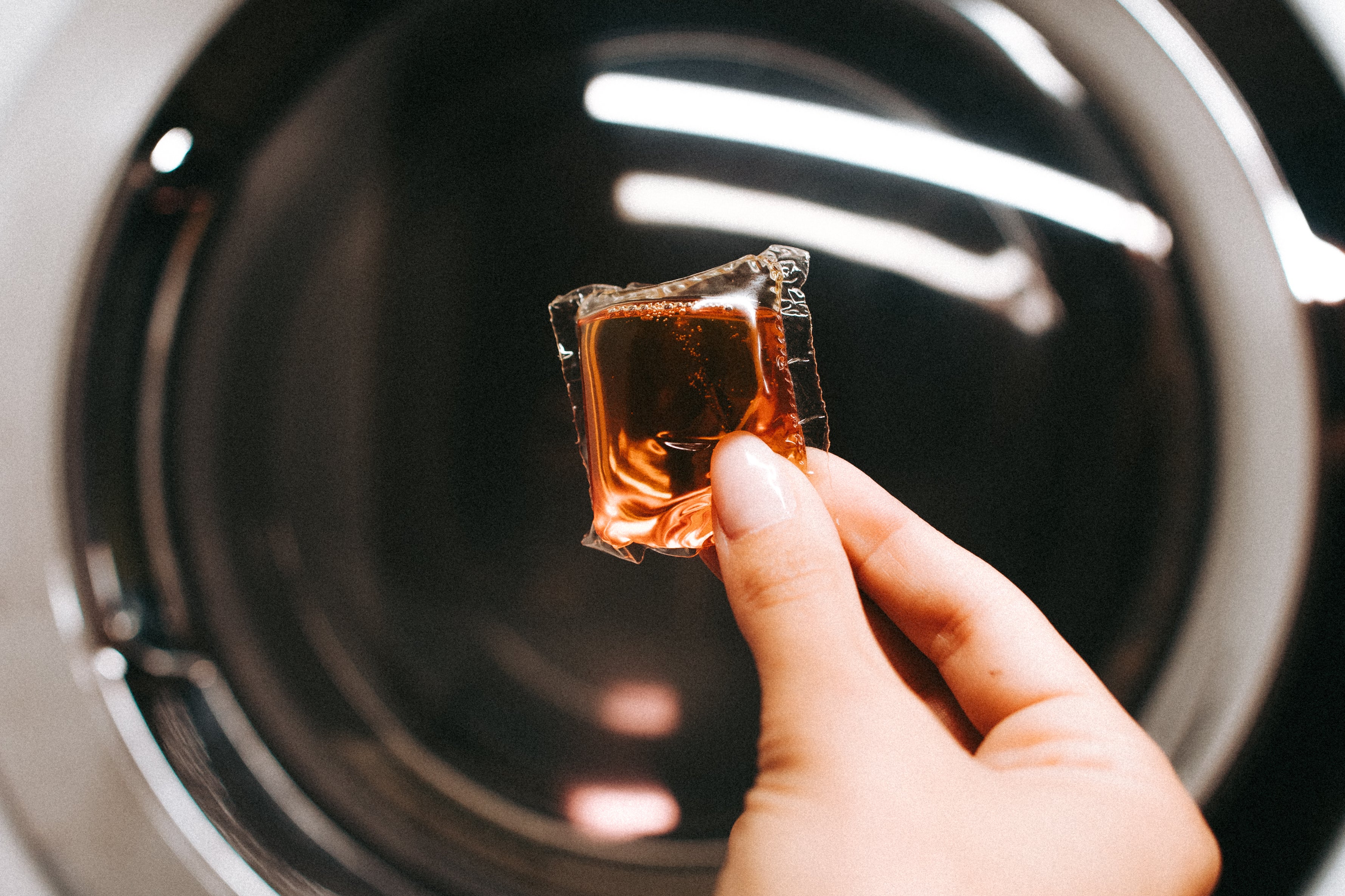 Hand dropping a Laundry Sauce Laundry Detergent Pod into a washing machine drum