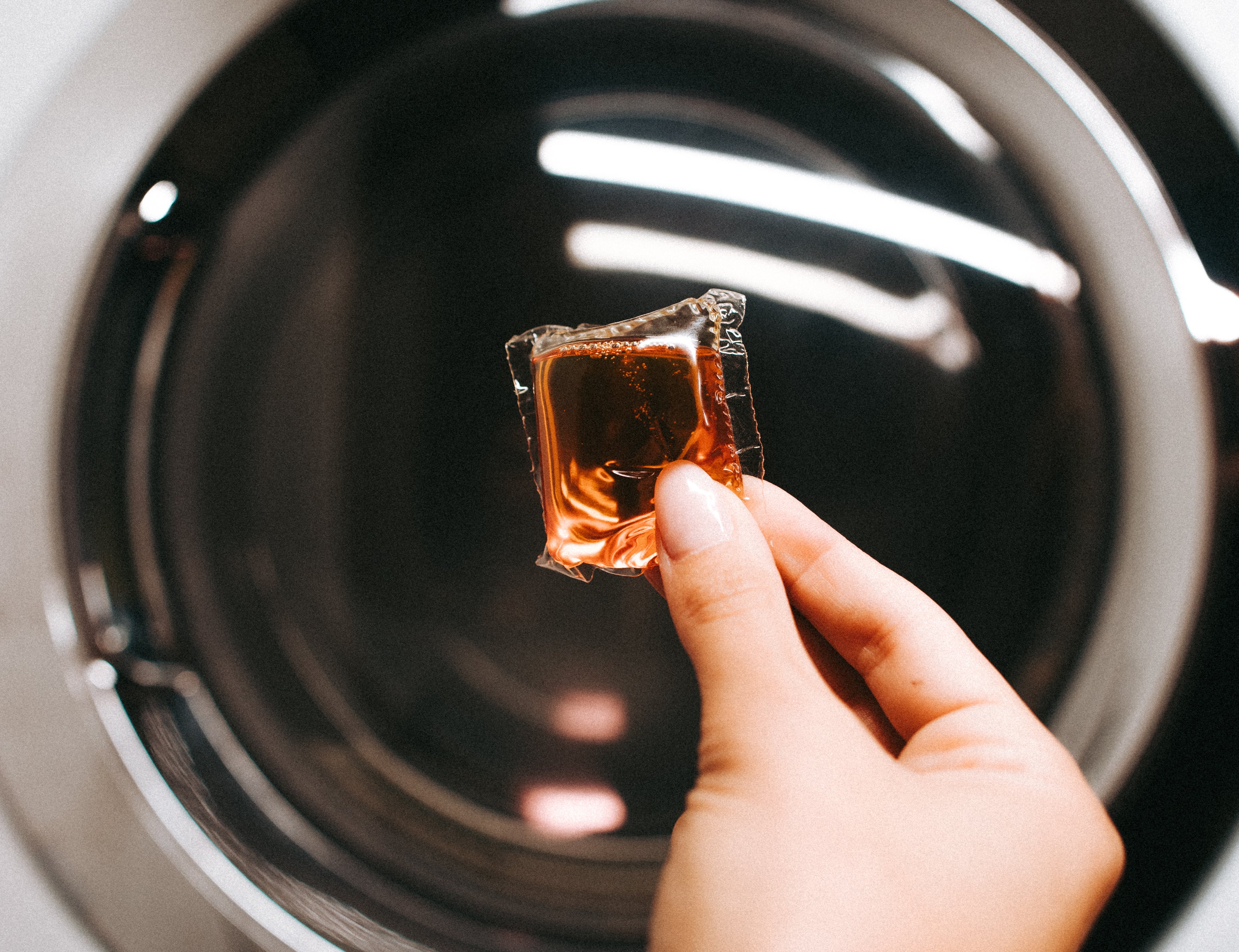 Hand dropping a Laundry Sauce Laundry Detergent Pod into a washing machine drum