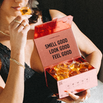 Woman holding an open pink box of Laundry Sauce Laundry Detergent Pods and smelling one