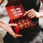 Woman in a black dress holding an open red box of Laundry Sauce Laundry Detergent Pods