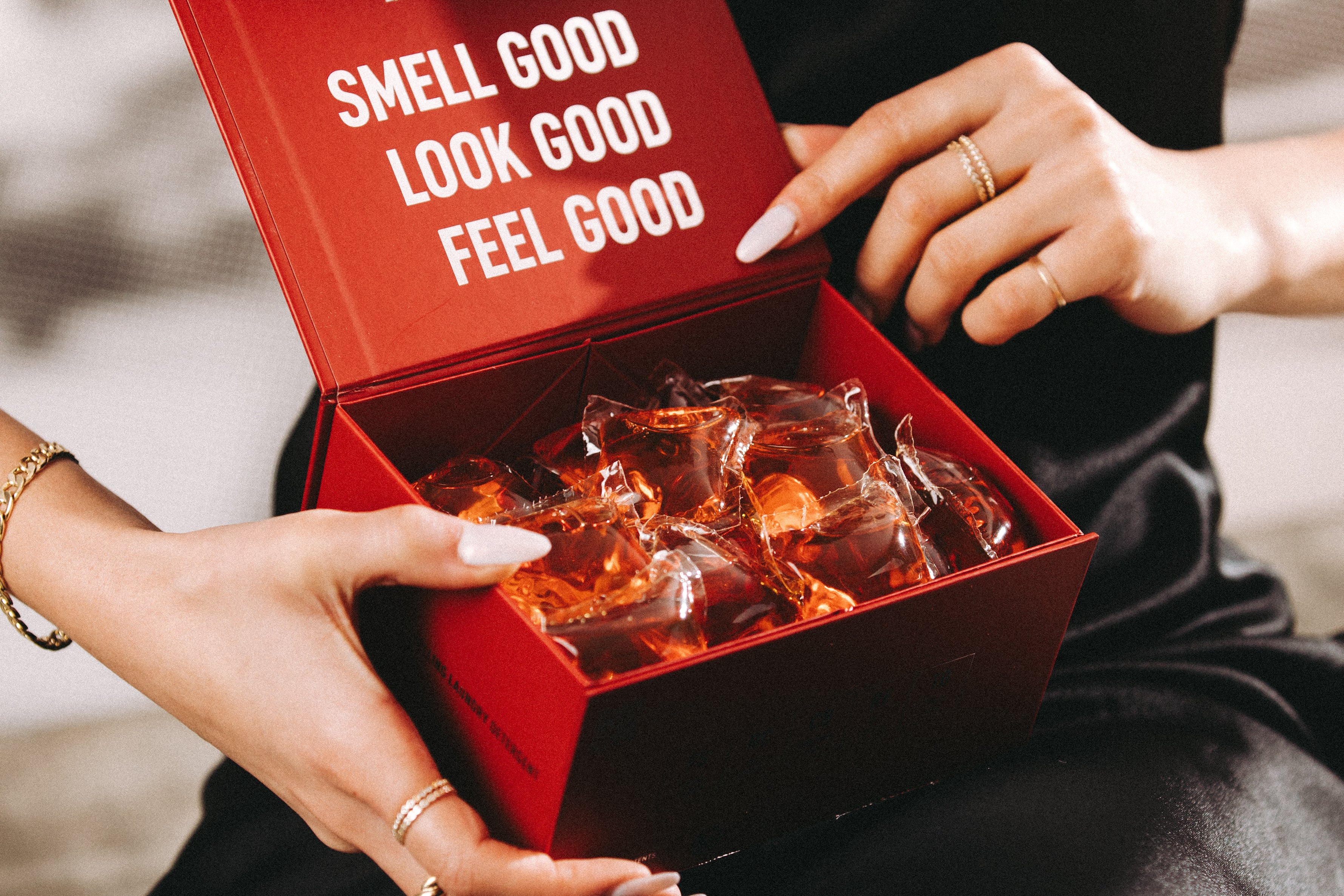 Woman in a black dress holding an open red box of Laundry Sauce Laundry Detergent Pods