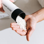 Hand pouring white Laundry Sauce Laundry Scent Booster beads from the canister into a palm