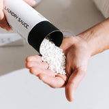 Hand pouring white Laundry Sauce Laundry Scent Booster beads from the canister into a palm